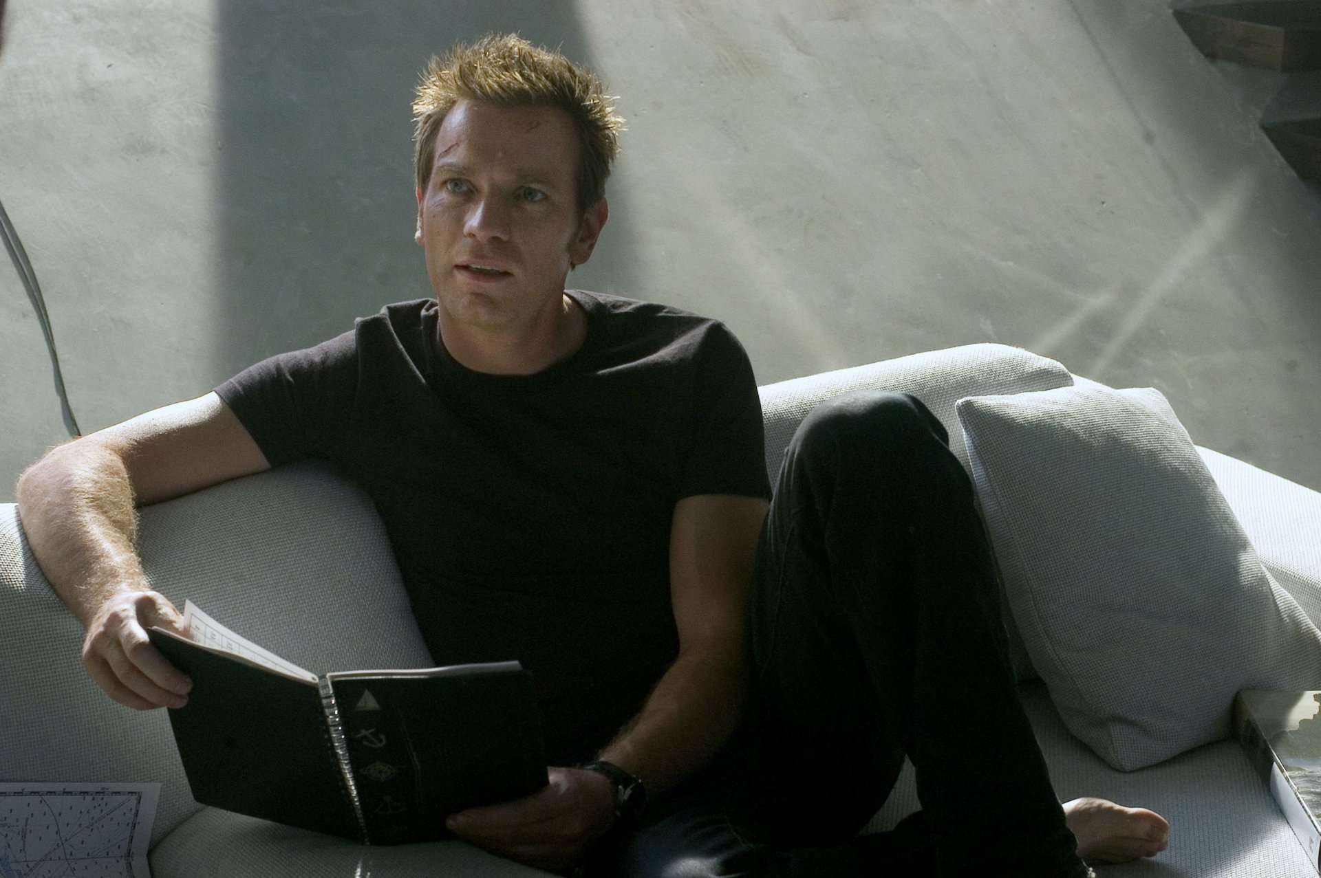 Cinematic 2K Quad HD PC desktop wallpaper: male actor reclining on a couch reading a notebook in a scene from the movie The Island.