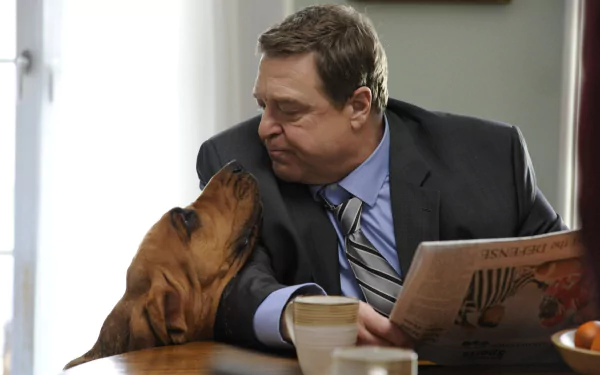 HD wallpaper from Alpha House featuring a man in a suit affectionately interacting with a dog while reading a newspaper.