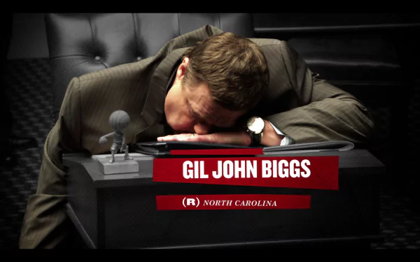 HD wallpaper of Alpha House featuring a character named Gil John Biggs resting his head on a desk with a nameplate.