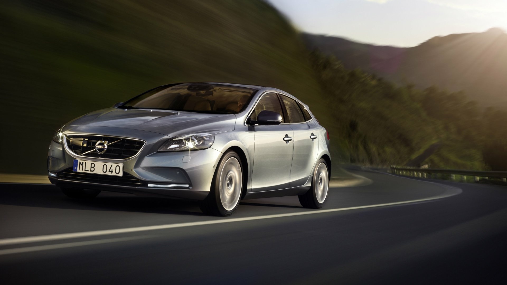 Silver Volvo V40 hatchback driving on a winding mountain road at dusk, motion-blur; 4K Ultra HD PC desktop wallpaper background of a Volvo vehicle.