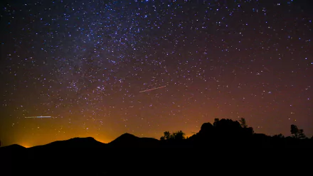 A stunning sci-fi scene featuring a starry night sky, highlighted by vibrant celestial patterns and silhouettes of distant mountains, captured in 4K Ultra HD for a captivating desktop background.