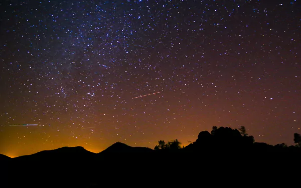 A stunning sci-fi scene featuring a starry night sky, highlighted by vibrant celestial patterns and silhouettes of distant mountains, captured in 4K Ultra HD for a captivating desktop background.