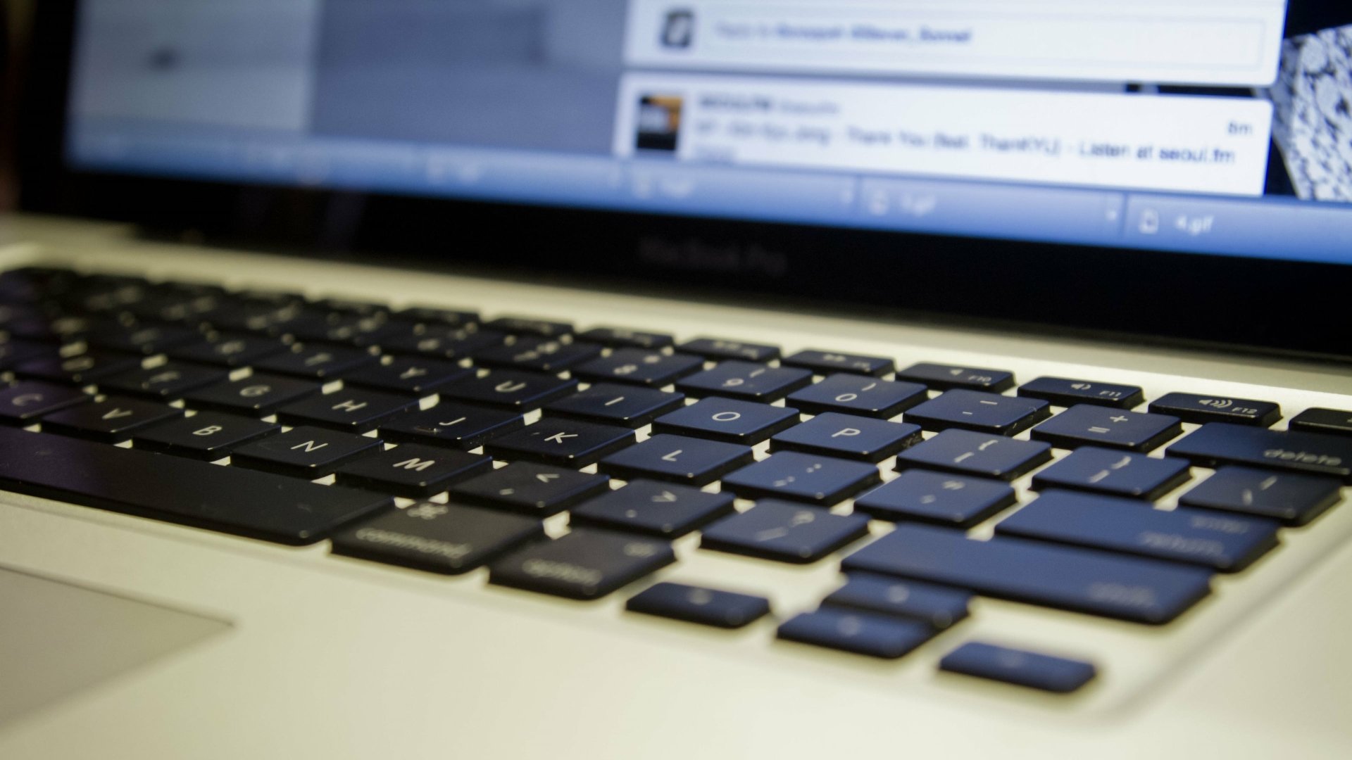 Close-up of a MacBook laptop keyboard with a blurred screen in the background, displayed in crisp 4K Ultra HD resolution showcasing modern technology.