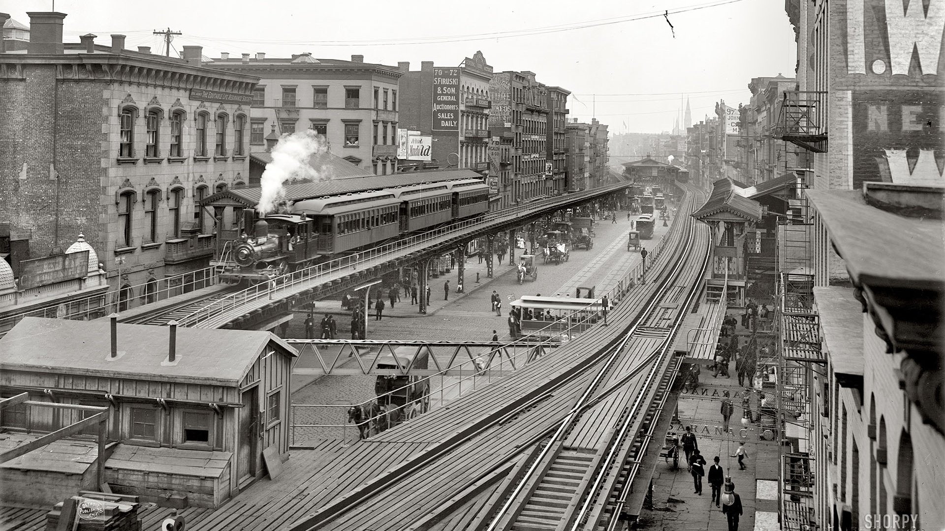 Black and white HD desktop wallpaper featuring a vintage steam train traveling on elevated tracks through an urban setting with surrounding buildings and pedestrians.