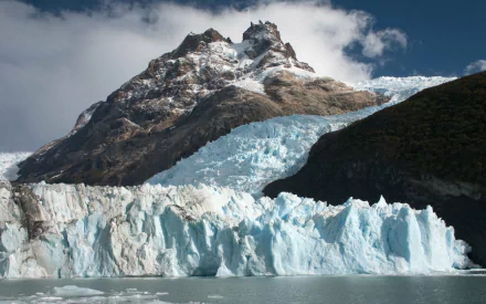 HD desktop wallpaper showcasing a stunning glacier and iceberg set against rugged mountain terrain under a partly cloudy sky, highlighting the beauty of nature.