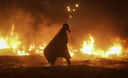 Silhouetted figure wearing a gas mask walks in front of intense flames and smoke in a dark, chaotic riot scene, captured in HD for a PC desktop wallpaper.