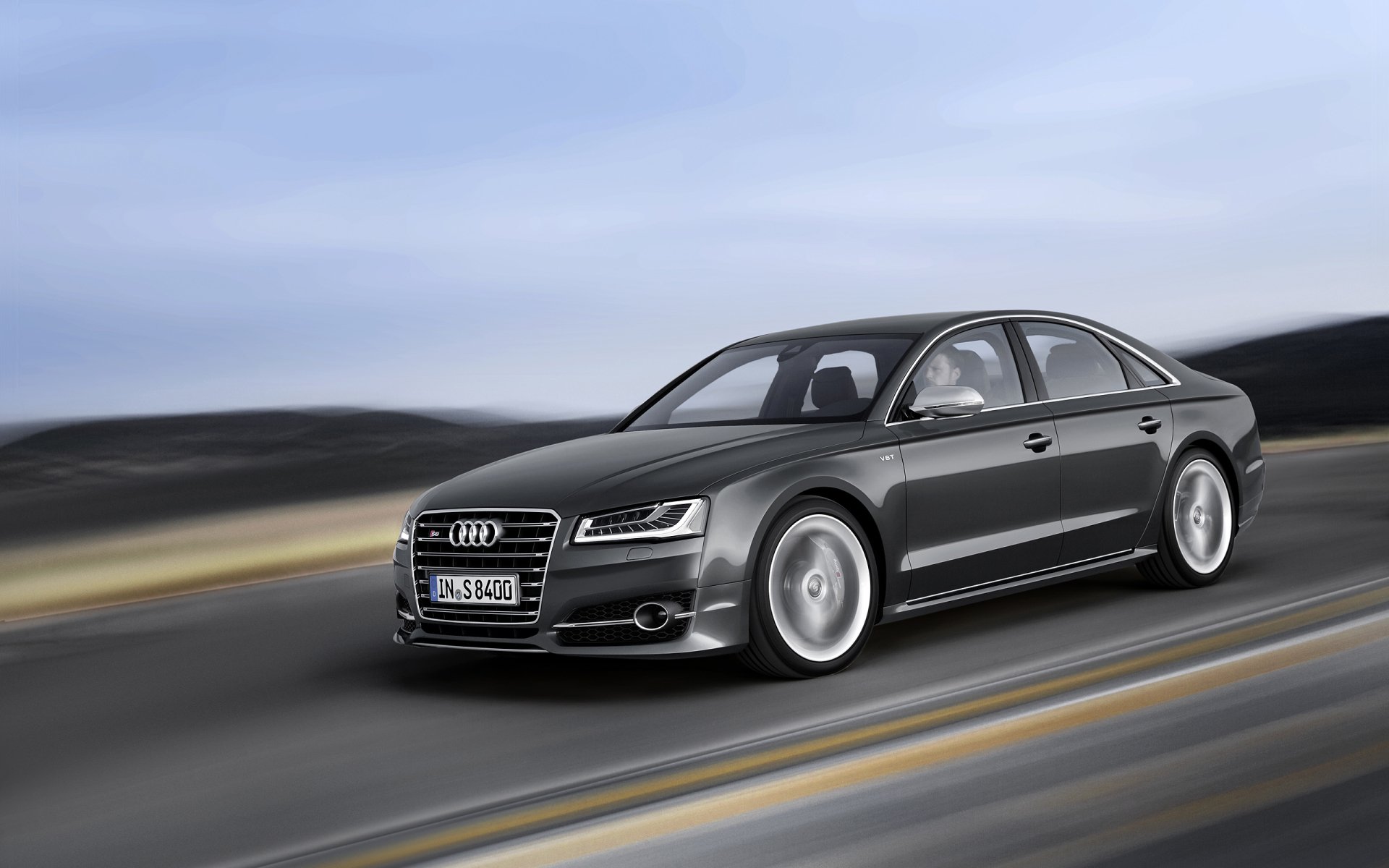 A sleek Audi A8 speeds along a scenic road, showcasing its elegant design and powerful presence, set against a blurred landscape for an HD desktop wallpaper.