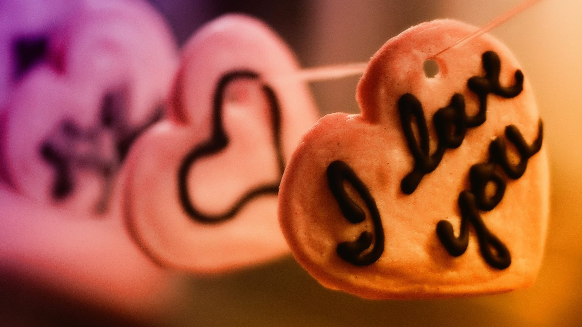 A close-up of heart-shaped cookies with I love you written on one, set against a softly blurred colorful background, makes for a charming artistic HD wallpaper celebrating love.