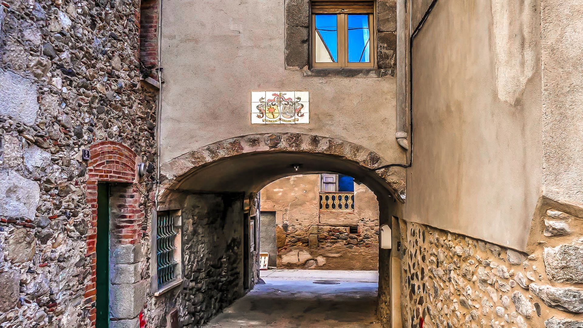 HD desktop wallpaper of a narrow man-made alley with stone and plaster walls, an arched passage, and a small window above, capturing rustic architectural details.