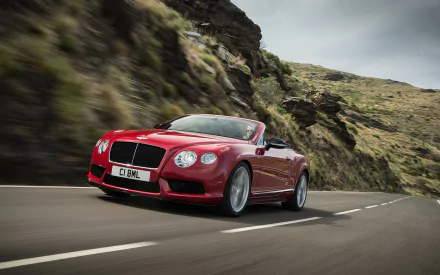 Red Bentley Continental GT V8 convertible driving along a winding mountain road — vehicle, 2K Quad HD PC desktop wallpaper and background.