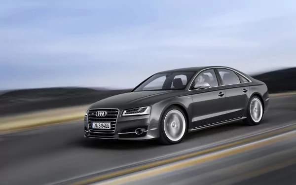 A sleek Audi A8 speeds along a scenic road, showcasing its elegant design and powerful presence, set against a blurred landscape for an HD desktop wallpaper.