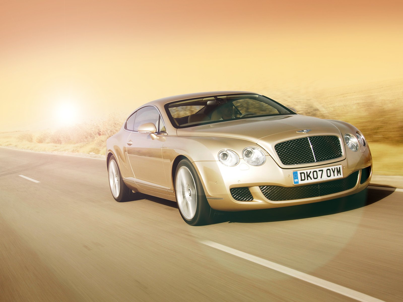 HD desktop wallpaper featuring a Bentley Continental GT Speed driving on a sunlit road, showcasing its sleek design and luxury performance.
