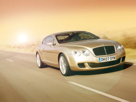 HD desktop wallpaper featuring a Bentley Continental GT Speed driving on a sunlit road, showcasing its sleek design and luxury performance.
