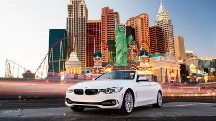 White BMW 4 Series Cabrio parked in front of a vibrant, illuminated cityscape resembling New York, captured as an HD PC desktop wallpaper background.