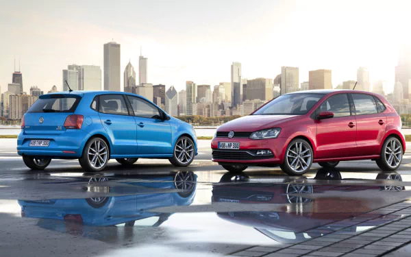 HD PC desktop wallpaper featuring two Volkswagen Polo vehicles, one blue and one red, parked on a reflective surface with a city skyline in the background.