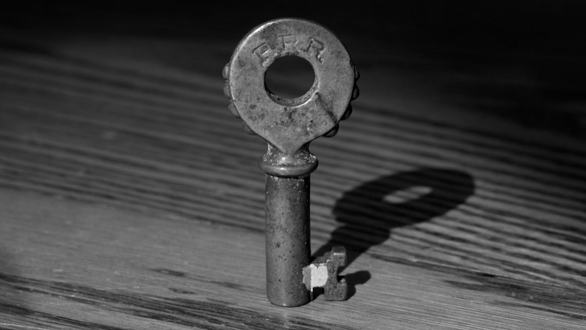 HD PC desktop wallpaper background: man-made vintage metal key standing upright on a wooden surface, casting a dark shadow.