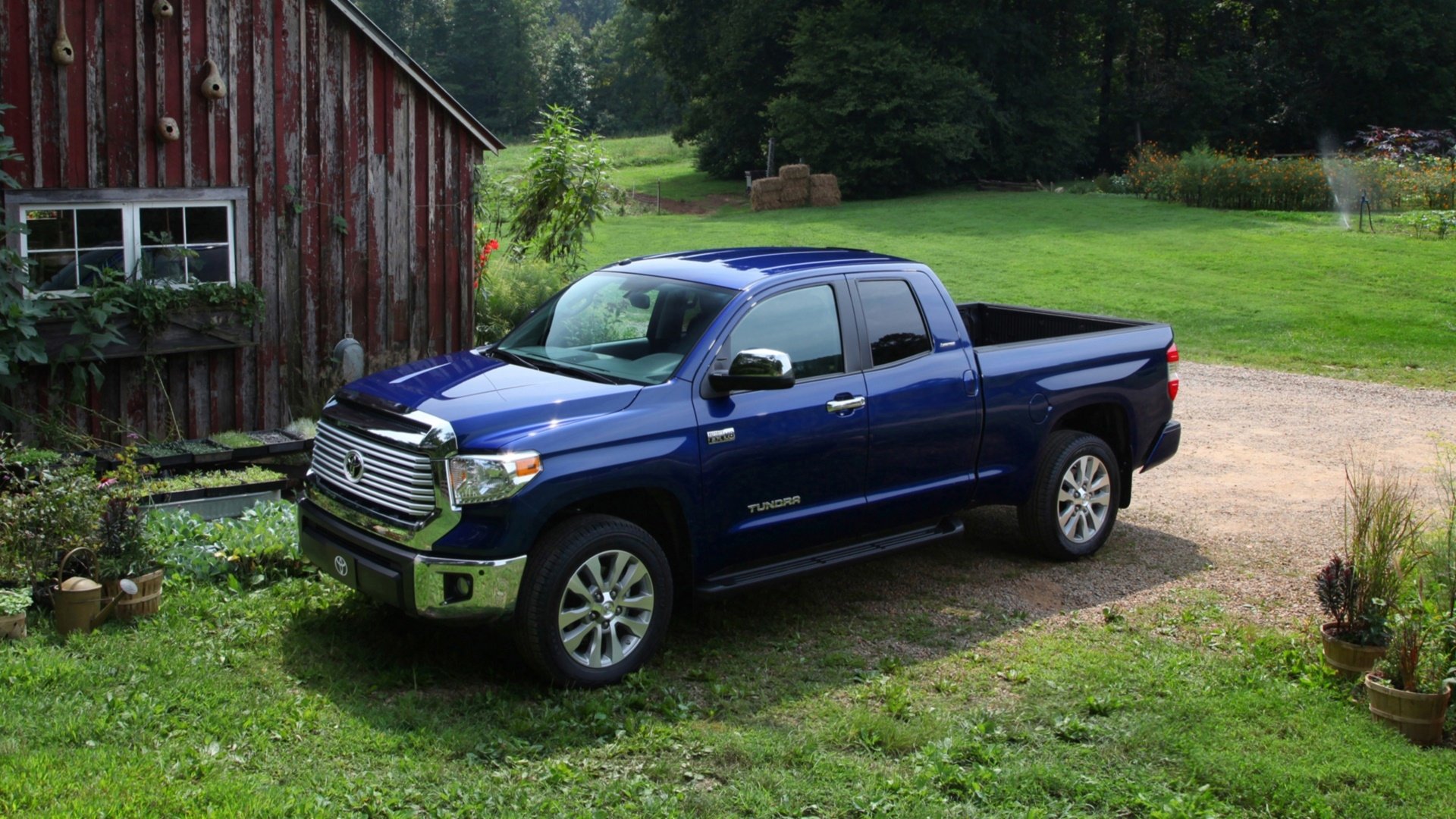 HD desktop wallpaper featuring a blue Toyota Tundra truck parked on grass next to a rustic red barn in a lush, green countryside setting.