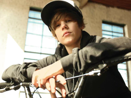 A high-definition desktop wallpaper of Justin Bieber, featuring him casually leaning on a bicycle in an indoor setting, exuding a cool and relaxed vibe.