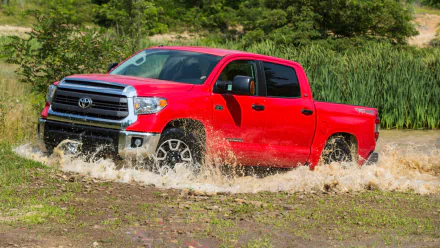 Red Toyota Tundra truck driving through a shallow, muddy water crossing in a green, forested outdoor setting; HD PC desktop wallpaper and background.