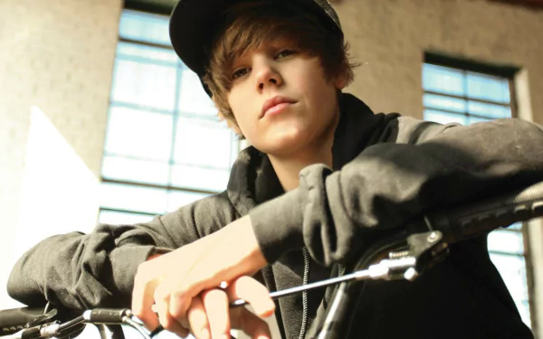 A high-definition desktop wallpaper of Justin Bieber, featuring him casually leaning on a bicycle in an indoor setting, exuding a cool and relaxed vibe.