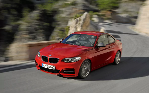Red BMW M235i Coupe speeding along a mountain road — vivid 2K Quad HD PC desktop wallpaper background of a BMW vehicle in motion.