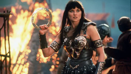 Xena: Warrior Princess HD desktop wallpaper features a fierce warrior holding a weapon, surrounded by a dramatic fiery background, capturing the show's adventurous spirit.
