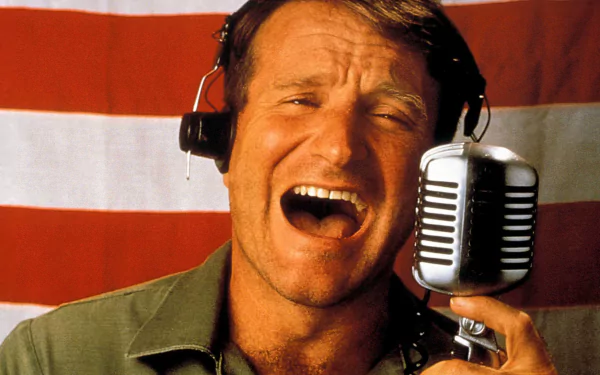 HD desktop wallpaper featuring a scene from Good Morning Vietnam with an expressive man in front of a microphone and an American flag background.