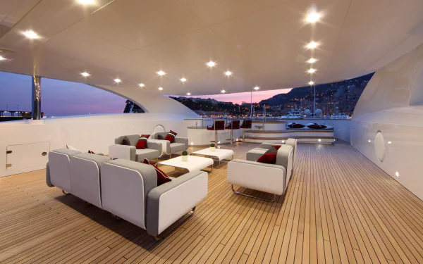 Spacious room on a luxury yacht with modern white seating, wooden deck flooring, and city lights visible at dusk, captured in 4K Ultra HD for a PC desktop wallpaper.
