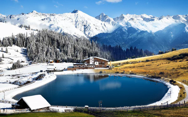 4K Ultra HD photography of a serene mountain lake surrounded by snow-covered peaks, evergreen trees, and a rustic lodge under a clear blue sky.