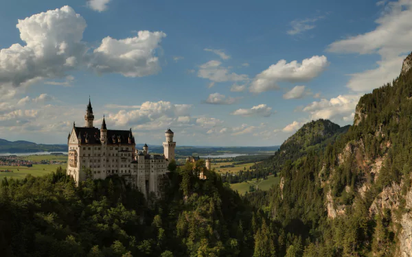 Neuschwanstein Castle, a majestic man-made structure, set against a scenic mountainous landscape under a partly cloudy sky, captured in stunning 4K Ultra HD.