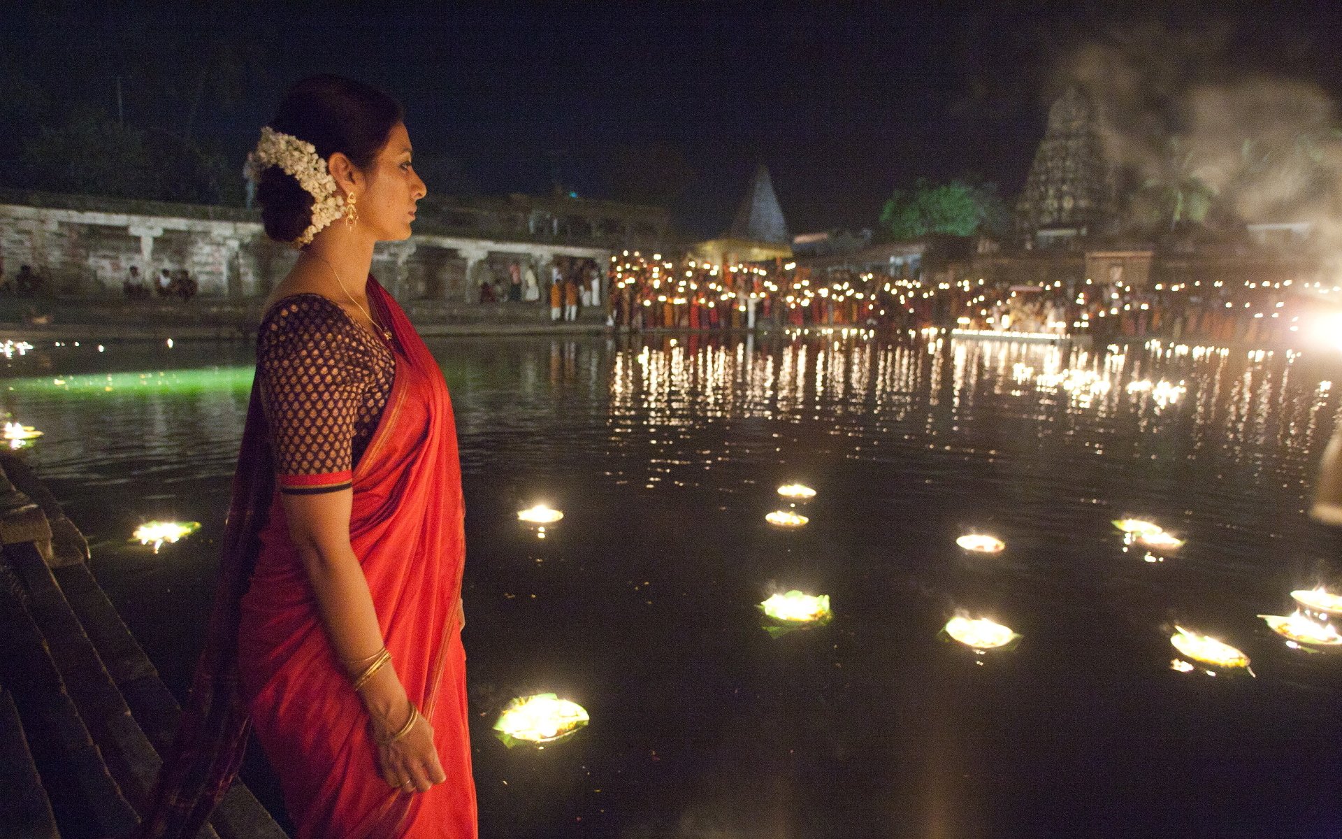 HD PC desktop wallpaper: Life of Pi scene — woman in a red sari watches floating lanterns drift across a river at night.