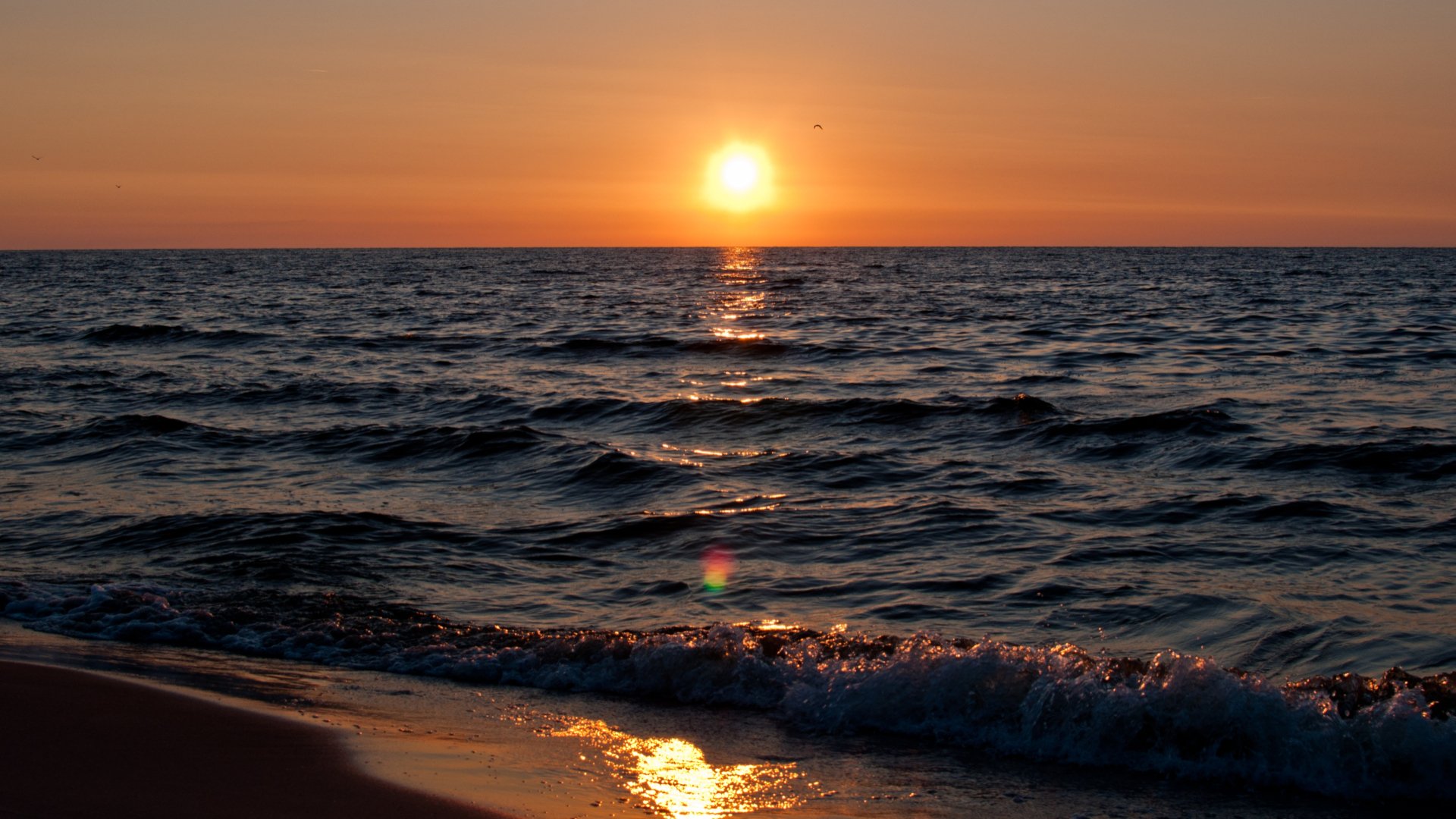HD PC desktop wallpaper: nature sunset with a golden sun over the ocean horizon, shimmering reflection on gentle waves and a sandy shoreline.