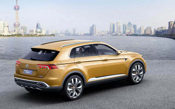 HD desktop wallpaper featuring a golden Volkswagen CrossBlue Coupe Twin Drive Concept vehicle parked by a waterfront with a city skyline in the background.