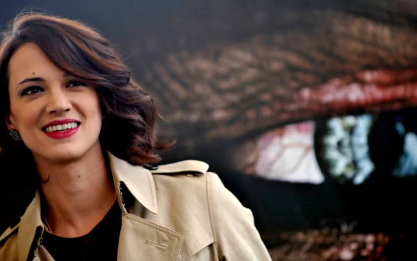 A captivating HD desktop wallpaper featuring Italian actress Asia Argento, smiling with a striking eye backdrop, showcasing her charisma and presence as a celebrity.