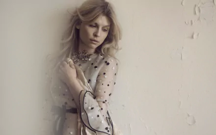 HD desktop wallpaper of a pensive woman styled like a French film actress in a sheer polka-dot dress, leaning against a textured pale wall under soft, diffused light.