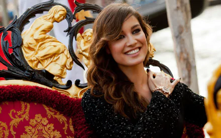 Smiling French woman in a black sequined dress seated on an ornate red-and-gold carriage; bright outdoor 2K Quad HD PC desktop wallpaper.