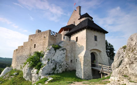 HD PC desktop wallpaper of man-made Bobolice Castle on a rocky hill, with stone walls and a wooden bridge beneath a clear blue sky.