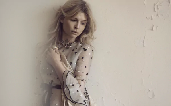 HD desktop wallpaper of a pensive woman styled like a French film actress in a sheer polka-dot dress, leaning against a textured pale wall under soft, diffused light.