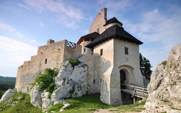 HD PC desktop wallpaper of man-made Bobolice Castle on a rocky hill, with stone walls and a wooden bridge beneath a clear blue sky.