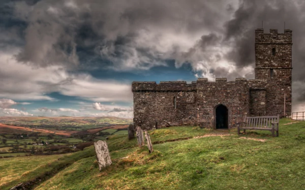 HD desktop wallpaper showing Brentor Church atop a grassy hill under dramatic, cloudy skies, embodying a striking religious and historic atmosphere.