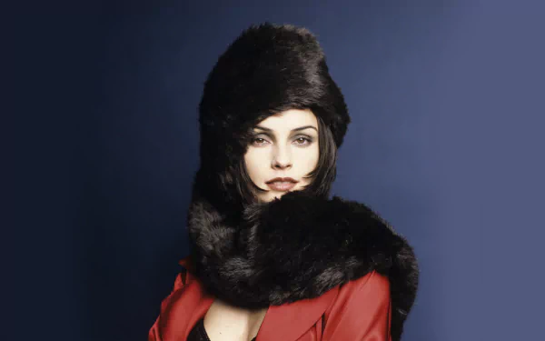 HD desktop wallpaper of Dutch actress Famke Janssen wearing a dark fur hat and matching scarf against a deep blue background.