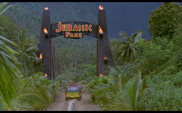A vibrant HD wallpaper featuring the iconic entrance to Jurassic Park, framed by lush greenery and a dramatic sky, setting the stage for an adventurous cinematic landscape.