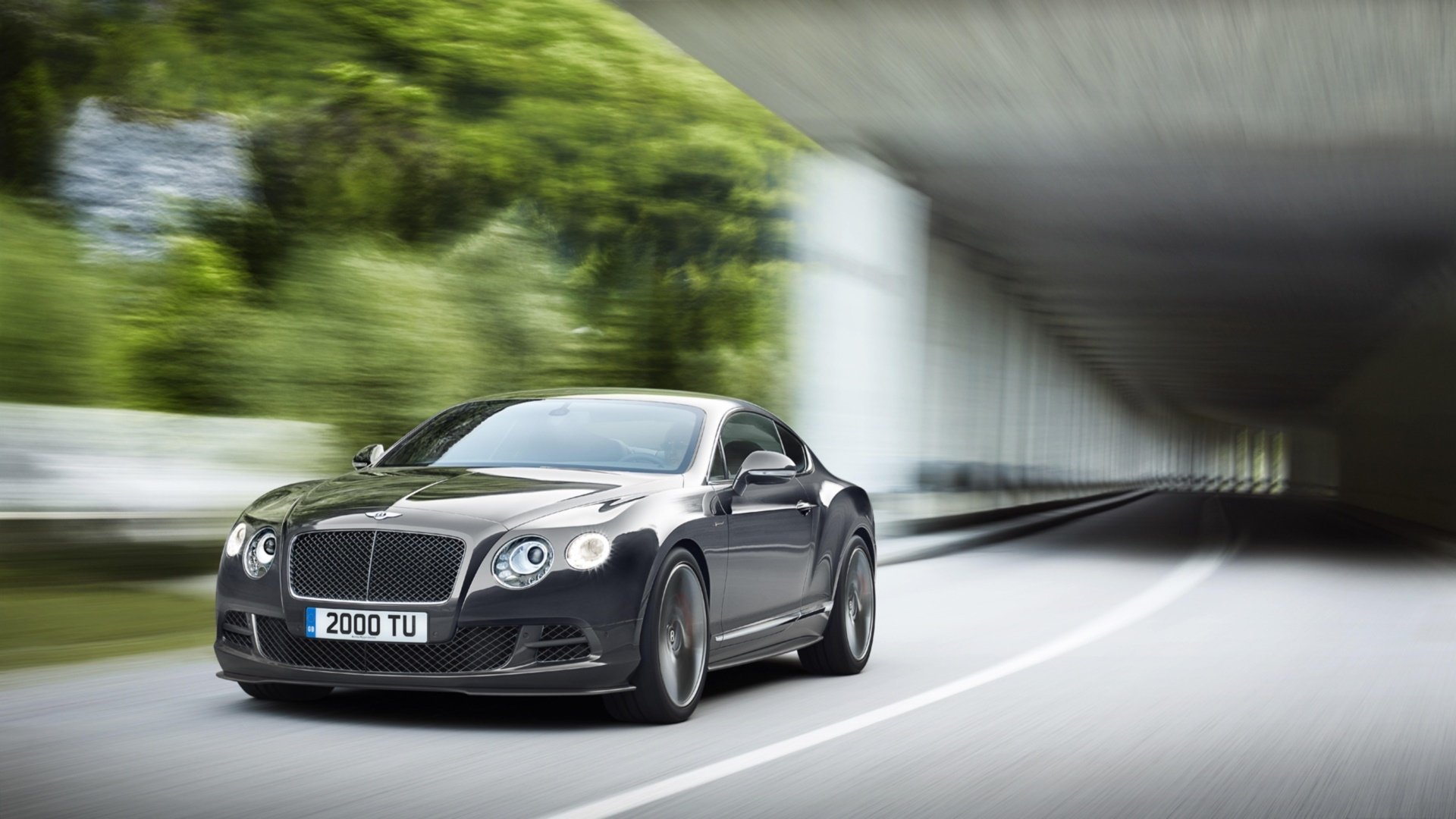 HD PC desktop wallpaper and background showing a black Bentley Continental GT Speed vehicle speeding through a blurred tunnel road with greenery.
