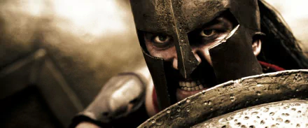 A fierce Spartan warrior from the movie 300 is shown in close-up, showcasing intense facial expressions and armor, making it a striking HD desktop wallpaper and background.