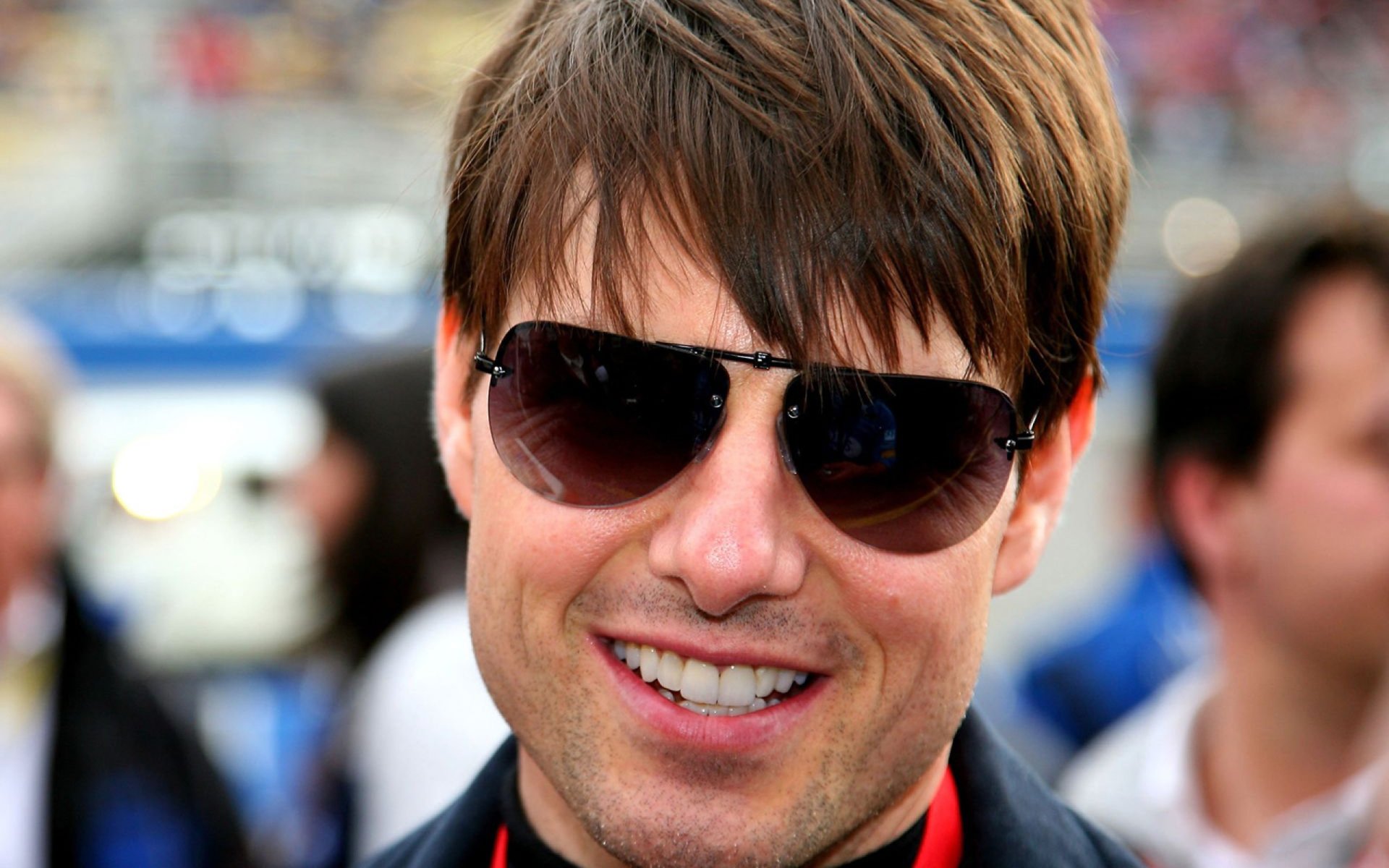 American actor Tom Cruise smiles while wearing sunglasses, captured at an event. This vibrant HD wallpaper features a close-up of the celebrity’s confident persona.
