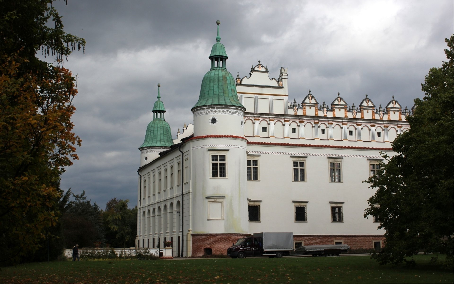 HD desktop wallpaper featuring Baranów Sandomierski Castle, a man-made historic structure with white walls and green spires under a cloudy sky.