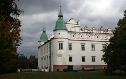 HD desktop wallpaper featuring Baranów Sandomierski Castle, a man-made historic structure with white walls and green spires under a cloudy sky.