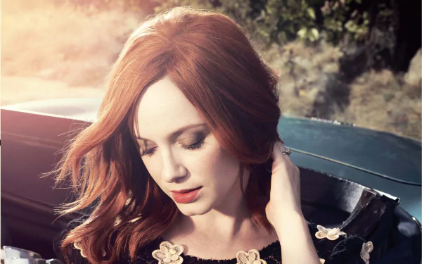 HD desktop wallpaper featuring American actress and celebrity Christina Hendricks with flowing red hair, gazing downward in a softly lit outdoor setting.