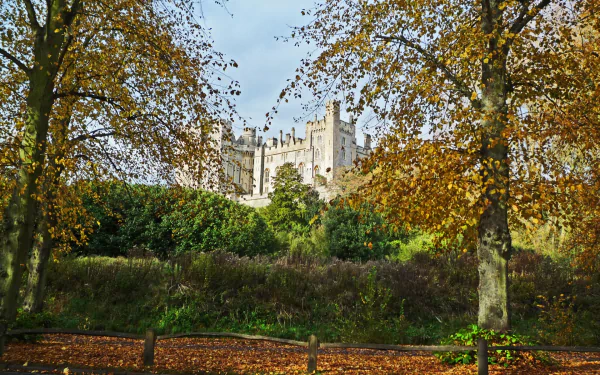 Arundel Castle rising above an autumn park, a man-made fortress framed by golden trees — HD PC desktop wallpaper/background.