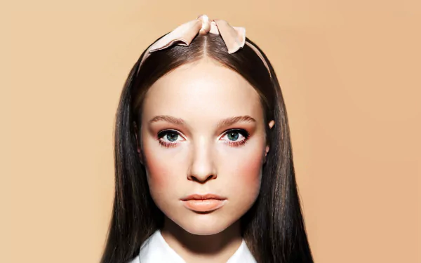 HD PC desktop wallpaper showing a French model woman with long dark hair, soft makeup and a pale ribbon headband, centered against a warm beige background.
